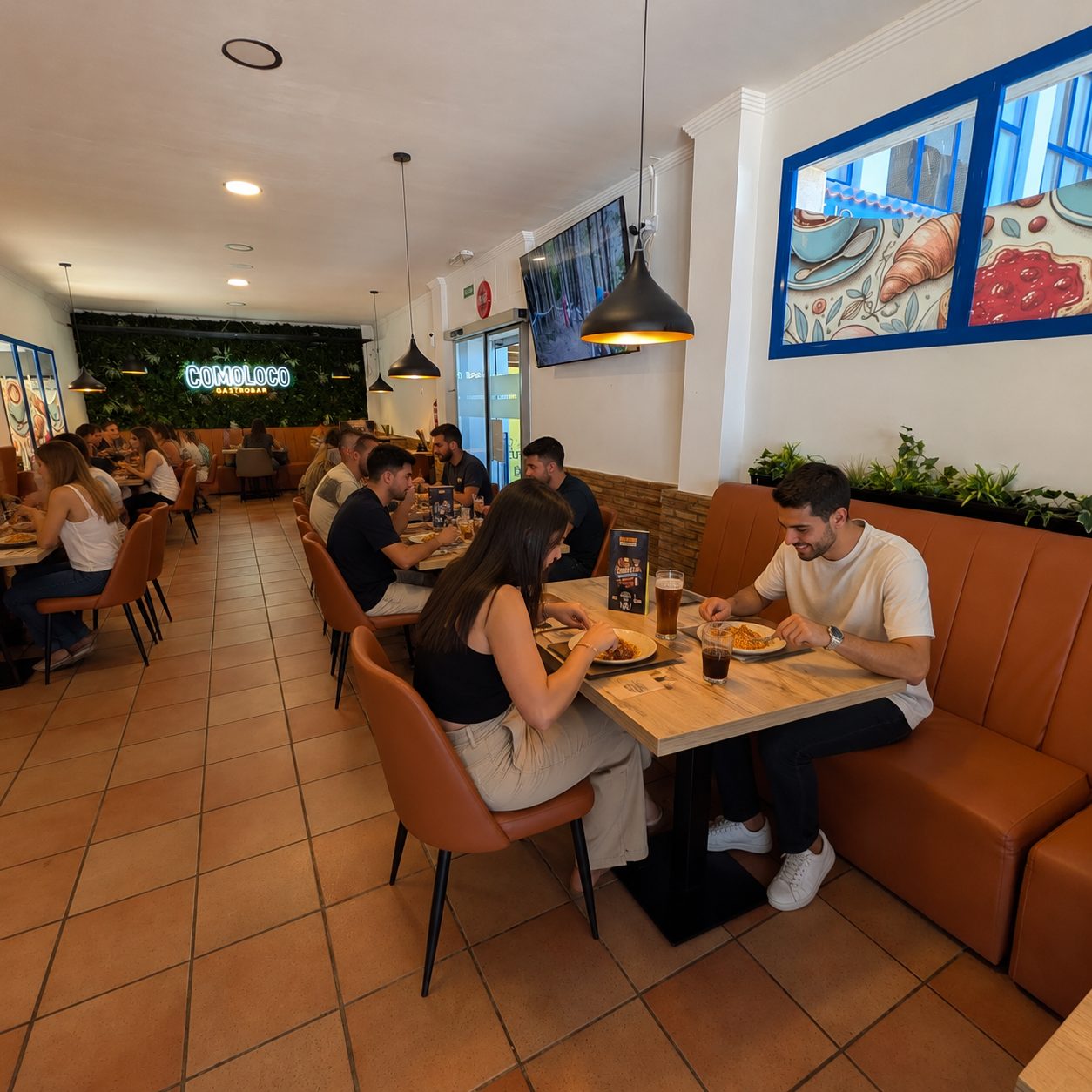 Interior del gastrobar con tapizado marrón, pared vegetal y cartel neón